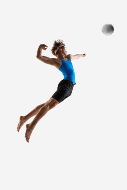 Voleybol oyuncusu, beyaz stüdyo arka planına karşı atletik formunu gösteren saldırı sırasında topa güçlü ve tam odaklı bir şekilde vurmak için zıplar. Şampiyonluk, maç, eylem, güç ve güç kavramı
