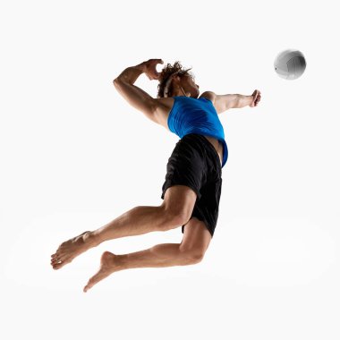 Genç adam, voleybol oyuncusu havanın ortasında çarpık bir poz vererek topa vuruyor ve beyaz stüdyo arka planına karşı tüm gücünü sergiliyor. Düşük açı. Eylem kavramı, güç, çeviklik, şampiyonluk