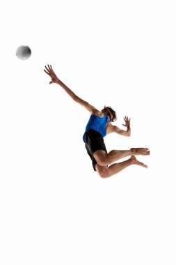 Mavi tişörtlü genç erkek voleybol oyuncusunun düşük açılı görüntüsü beyaz stüdyo arka planına karşı zarif duruş ve enerjiyle topu parçalamak için zıplıyor. Spor kavramı, şampiyonluk, atlama, hareket