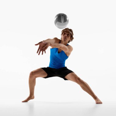 Adamım, voleybol oyuncusu kollarını ileri açıp beyaz stüdyo arka planına karşı tüm dikkatini vererek top resepsiyonuna hazırlanıyor. Spor oyunu konsepti, şampiyonluk, hareket