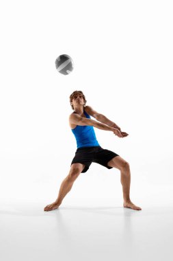 Voleybol atleti gözünü toptan ayırmıyor ve klasik pozlarda kollarını bir araya getirip beyaz stüdyo arka planına karşı oynuyor. Oyuncu odaklanmış görünüyor. Spor anlayışı, şampiyonluk, disiplin