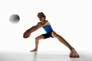 Geniş duruşlu odaklı voleybol oyuncusu, beyaz stüdyo arka planına karşı sıkı kolları ve ciddi yüzüyle topu almaya hazırlanıyor. Düşük açı. Spor şampiyonası konsepti, rekabet, hareket