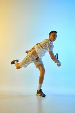 Şık giyinen erkek tenisçi, sıcak neon ışıkta mavi-sarı renkli arka planda tam kıvrımlı poz veriyor. Yetenek kavramı, momentum, hareket