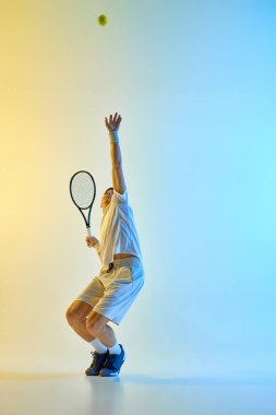 Tenis oyuncusu raketle uzanarak, sıcak neon ışıkta renkli mavi-sarı gradyan arkaplana karşı servis yapmaya hazırlanıyor. Spor kavramı, maç, odaklanma, beklenti, hareket