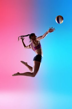 Atletik bayan oyuncunun voleybol topuna uzanan yan görüntüsü havada yükselirken gradyan arkaplana karşı canlı çift tonlu ışıklandırma ile. Eylem kavramı, hassasiyet, spor yarışması.