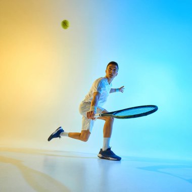 Turnuva hareketlerinde genç tenisçi, raketle dönüyor ve neon ışıkta koyu mavi-sarı renkte bir arka plana karşı iz sürüyor. Spor anlayışı, çeviklik, hareket, enerjik oyun