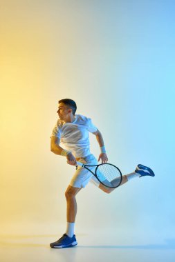 Tarz sahibi tenis oyuncusu, sıcak neon ışıkta renkli mavi-sarı gradyan arka plana odaklanmış bir ifadeyle salıncak adımını tamamlıyor. Spor etkinliği kavramı, maç, hazırlık, eylem
