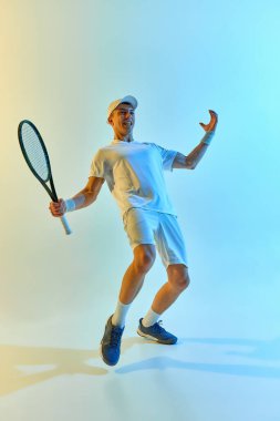 Tenis oyuncusu galibiyeti kutluyor, zaferle gülümsüyor ve parlak mavi-sarı renkli arka planda sıcak neon ışıkta sevinçle yumruğunu sıkıyor. Başarı kavramı, amaç, kazanmak