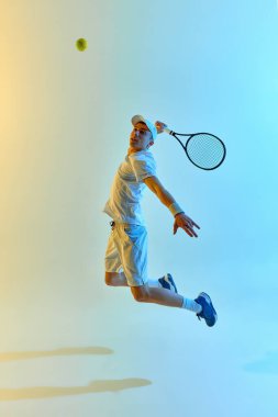 Zıplayan tenisçi havada salıncağın ortasında yakalandı, sıcak neon ışıkta canlı mavi-sarı gradyan arka planda servis için tamamen genişletildi. Dinamik hareket kavramı, spor etkinliği, atletik güç.