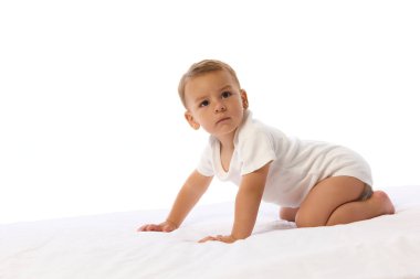 Sürünen küçük çocuk beyaz stüdyo arka planına karşı yumuşak yatağa odaklanmış şekilde yukarı bakıyor. Gelişim, hareket, çocukluk, güç, kararlılık, keşif kavramı..