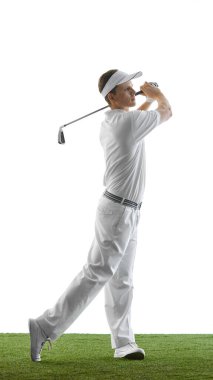Kenar manzaralı bir fotoğrafta, güçlü bir golf vuruşunu kendinden emin bir şekilde bitiren, beyaz spor kıyafetler giyen ve yeşil çimlerin üzerinde beyaz arka planda güneşlenen bir adam görülüyor. Enerji kavramı, disiplin, geleneksel spor