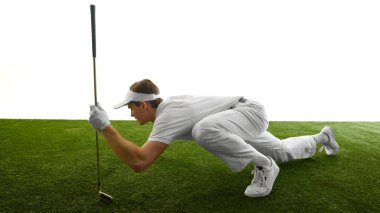 Top pozisyonunu kontrol etmek için çömelmiş, golf sopasına yaslanmış, stüdyo ortamında tamamen beyaz üniforma giymiş bir adamın yan görüntüsü. Enerji kavramı, golf ritüeli, oyun, spor odaklanma, sabır