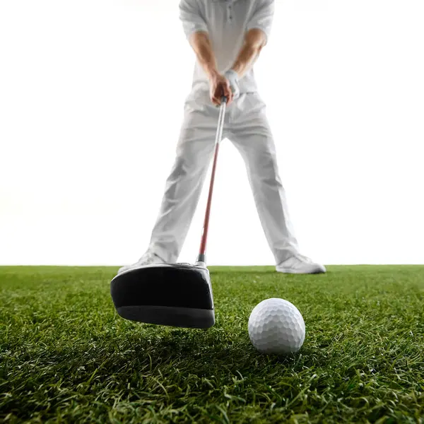 Yakından, topa vurmaya hazırlanan adamın düşük açılı görüntüsü, golf sopası başı ve topu keskin bir şekilde yeşil çimlere odaklanmış. Golf, lüks, oyun başlangıcı, güç, zamanlama, spor yoğunluğu kavramı