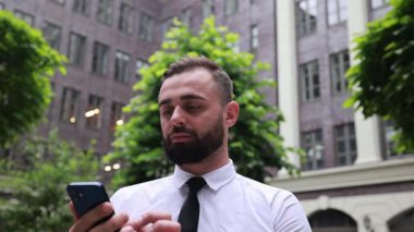 Resmi takım elbiseli bir işadamı iş bölgesinde dışarıda duruyor, elinde akıllı bir telefonla video görüşmesinde konuşuyor. Mobil toplantı kavramı, sanal iletişim, liderlik.