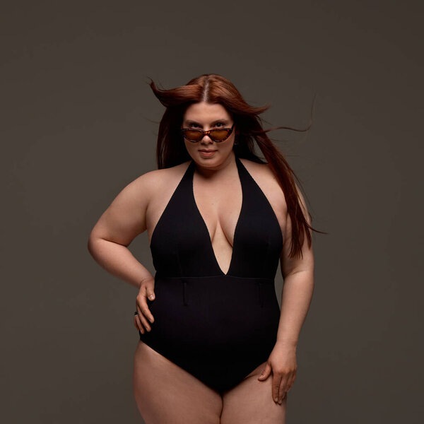 A plus-size model confidently poses in a stylish black swimsuit, embodying empowerment and modern fashion. Concept of self-love and body positivity in contemporary fashion.