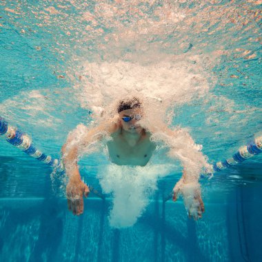 Bir su altı görüntüsü yüzücülerin dinamik hareketlerini yakalar ve açık mavi bir havuzda kabarcıklar oluşturur. Su sporları ve hareket dinamiği kavramı.