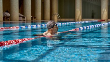 Bir yüzücü kapalı havuzun kenarında mola verir, yan tarafındaki şerit işaretleri ve şık sütunlarla. Atletizm ve modern mimari kavramı.