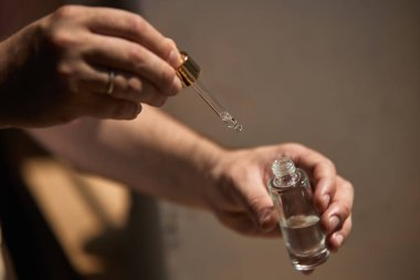 Melez cilt bakımı. Bir çift beyaz el, içinde temiz sıvı bulunan bir cam damlacığı ve küçük bir şişe tutuyor. Temel yağlar veya cilt serumu uygulaması kavramı.