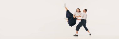 İki kişi enerjik bir lindy hop dansı yapıyor ve beyaz bir stüdyonun arka planında dinamik pozlar veriyor. Dans ve hareket yoluyla neşeli ifade kavramı. Pankart