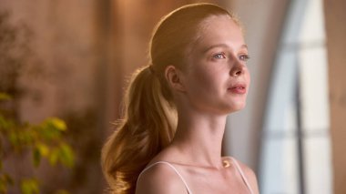 Seçkin güzellik. Sakin bir ifadeye sahip genç bir kadın yemyeşil bir pencerenin yanındaki yumuşak ışıklı bir odada duruyor. İçerideki sakinlik ve doğa kavramı.