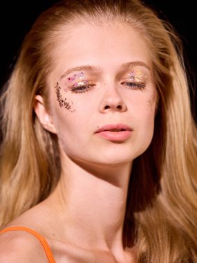 Cesur Y2K. Yaratıcı parıltı makyajlı genç bir kadın, sakin bir ifade sergileyerek hafif ışıklandırmayla aydınlatılır. Sanatsal güzellik ve dingin zarafet kavramı.