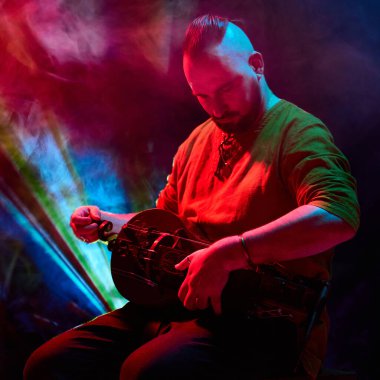 Bir müzisyen canlı kırmızı ve mavi sahne ışıkları altında ustaca hurdy-gurdy çalar. Benzersiz müzik performansları ve atmosferik sahne aydınlatma efektleri kavramı.