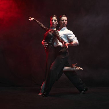 Zarif bir çift tutkulu bir Arjantin tango pozu veriyor, dramatik kırmızı ışıkla kaplanmış. Canlı duygu ve zamansız dans sanatının kavramı.