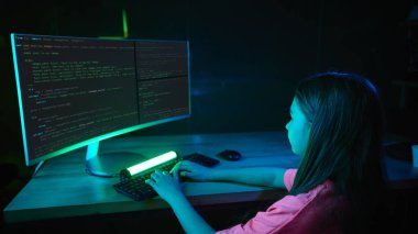 Karanlık bir odada, parlayan neon ışıkları ve bilgisayarında kod olan bir klavyede yazan bir kız. Ekranda sahte kodlama. Programlama eğitimi kavramı, gelecekteki iş ortamları