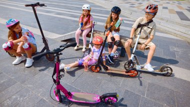 Yudumla ve rahatla. Çocuklar açık hava eğlencesinin tadını çıkarmak için parlak yaz güneşinin altında scooterlarını sürmeye can atıyorlar. Bu, neşeli çocukluk özgürlüğü kavramını somutlaştırıyor. Grup aktiviteleri ve fiziksel sağlık