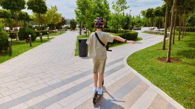 Çocuk sürücü. Güvenlik kaskı takıyor, güneşli bir parkta scooter sürüyor, açık hava güvenliği ve eğlence fikrini temsil ediyor..