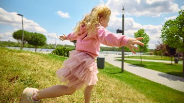 Yandan koşma parıltısı. Neşeli çocuk açık mavi gökyüzünün altındaki parkta koşar, mutluluk ve kaygısız ruh yayar, çocukluk özgürlüğü kavramı, saf enerji ve doğal oyun zamanı hareketi.