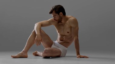 Beyaz iç çamaşırlı kaslı erkek model gri arka plana bakıyor. İncinebilirlik, içgözlem ve moda içinde sessiz erkeksi duygu kavramı.