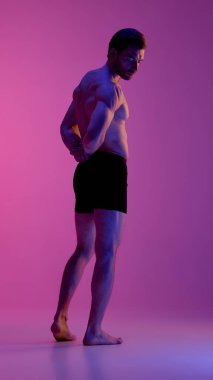 Pembe ışığın altında siyah boxerlı stüdyo adamı yan yan duruyor. Duygusallık kavramı, erkek modası, beden estetiği, kontrast aydınlatma, duygusal içgözlem.