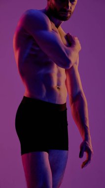 Atletik adam, fiziğinin altını çizen çarpıcı ışıklandırma altında şık iç çamaşırlarıyla poz veriyor. Duygusallık kavramı, erkekler moda, beden estetiği, kontrast aydınlatma, duygusal içgözlem.