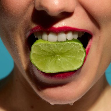 Yakından gülümseyen kadın, parlak dudaklarında kırmızı rujla limon dilimini ısırıyor. Turunçgil tazeliği, güzellik eğilimleri, cilt bakımı, şehvet ve yaz reklam kampanyaları kavramı.