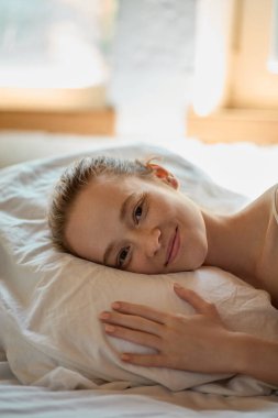 Huzurlu, genç bir kadın, yumuşak, doğal bir ışıkla yastığa baş koyuyor. Dinlenme, sağlık, duygusal rahatlık, yumuşaklık, yaşam tarzı, cilt bakımı ve güzellikle ilgili içerik kavramı.