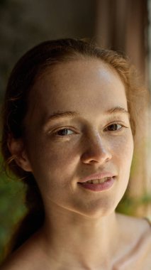 Yüzünde çilli ve rahat bir ifade olan düşünceli genç bir kadının doğal hafif portresi. Medyada özgünlük, doğal güzellik, sağIık, cilt bakımı ve duygusal berraklık kavramı.