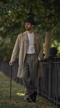 Antika elbiseli bir adam ağaçların altındaki demirden bir çitin yanından geçiyor. Çağdaş fotoğraf sergileri, galeri kurulumları ve kavramsal seriler için sahnelenmiş duygusal portreler kavramı