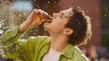 Islak saçlı yeşil gömlekli adam çarpıcı bir şekilde su altında hamburger yiyor. Abartılı açlık kavramı, fast food tutkusu, gençlik draması, yaz pazarlama görselleri.