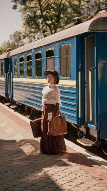 Tren peronunda bavul ve gazeteyle bekleyen şapkalı ve klasik etekli bir kadın. Kurgu kapağı kavramı, geçmişe dönük şehir seyahati, psikolojik anlatım, dönem drama serisi posteri