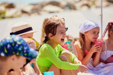 Çocuklar sahilde içkiler ve kahkahalarla güneşli bir günün tadını çıkarıyorlar. Duygusal öğrenme araçları kavramı, anaokulu sosyal davranış materyali, çocuk grubu aktiviteleri, neşe dolu yaz mevsimi