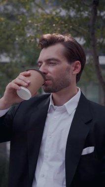 Açık hava molası. Takım elbiseli bir işadamı şehir parkında kahve içiyor. Uzak iş hayatı kavramı, açık hava kahve molası, modern iş modası, şehir ortamında zihinsel şarj.