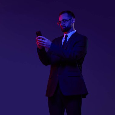 Koyu renk takım elbiseli bir iş adamı mavi ve kırmızı ışıkta akıllı telefon kullanıyor. Dijital güvenli, kişisel finans uygulaması pazarlama ve mobil-ilk fintech platform tanıtımı kavramı.