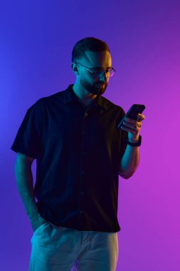 Gözlüklü adam, parlak mor ve mavi ışık arka planına karşı akıllı telefon okuyor. Dijital yaşam tarzı markalaşması, hareket halindeki mobil bankacılık kavramı ve teknoloji meraklısı kullanıcılar için gevşetilmiş UX tanıtımı.