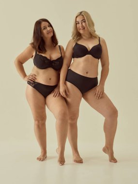 Siyah iç çamaşırlı, tarafsız arkaplanda poz veren kendine güvenen kadınlar. Vücut güveni, kadın arkadaşlığı, iç çamaşırı pazarlaması ve modern güzellik standartları kavramı..
