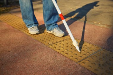 Kaldırımda köre rehberlik eden dokunsal asfaltta beyaz baston. Kentsel erişim kavramı, yardımcı araçlar, kapsayıcı tasarım ve görme engelliler için hareketlilik eğitimi.