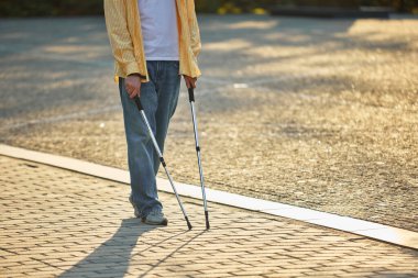 Koltuk değnekleriyle şehir güneşinde kaldırımda yürüyen bir adam. Kentsel erişilebilirlik kavramı, asist teknoloji, sosyal kapsama ve farkındalık kampanyaları.