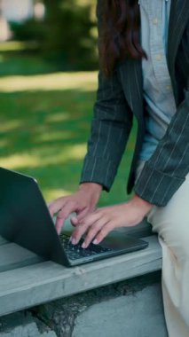 İş kadını dışarıda ahşap bankta çalışırken dizüstü bilgisayarda daktilo kullanıyor. Profesyonel iletişim, ticari görevler, serbest projeler, mobil çalışma alanı ve esnek kariyer yaşam tarzı kavramı.