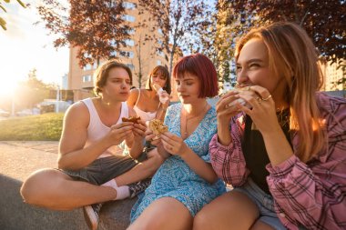 Bir grup arkadaş sıcak gün batımında birlikte sokak yemeklerinin tadını çıkarıyorlar. Fast food reklamcılığı, gençlik yaşam tarzı, sosyal medya, festivaller, sağlıklı denge ve şehir turizmi kavramı.