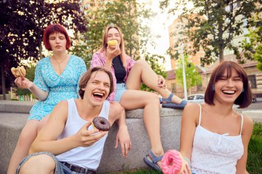 Güneşli bir günde dışarıda gülen ve renkli çöreklerin tadını çıkaran bir grup arkadaş. Arkadaşlık kavramı, eğlence, sokak yemekleri, yaz eğlencesi ve neşeli sosyal etkileşim..